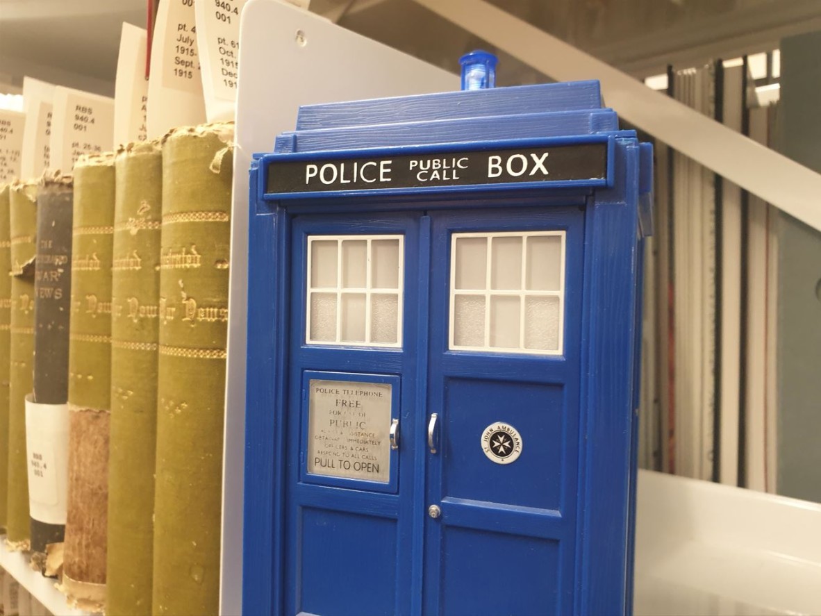 A toy TARDIS sitting on the shelf next to several old books