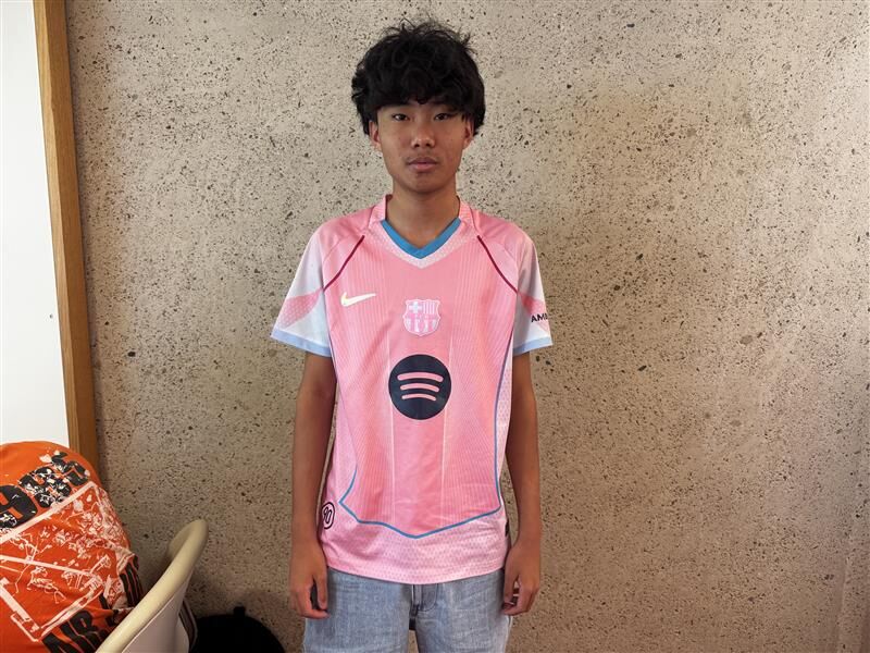 A photo of a young person standing against a concrete wall in pinks sports jersey
