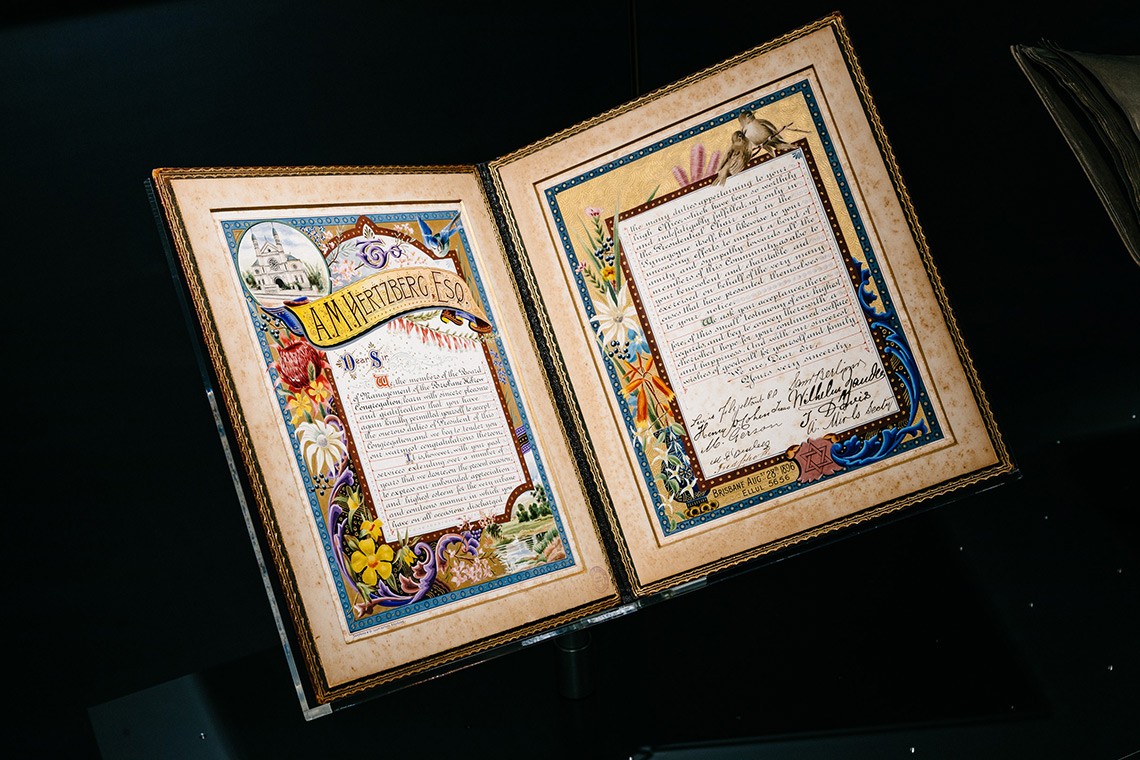 An illuminated address presented to Adolphus Hertzberg, President of the Brisbane Hebrew Congregation, in 1896. The illuminated address is contained in an olive coloured leatherbound, gold embossed album with silver insignia. The inner pages feature an illustration of the Brisbane Synagogue and borders containing birds and flowers decorated with gold and silver.