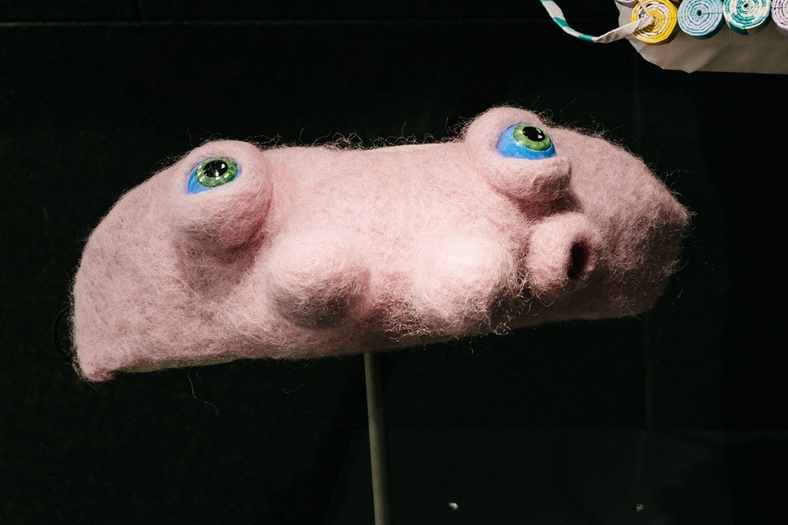 The Covid 19 mask “Alienation” is a “reflection on a shift from feelings of anxiety to curiosity and hope during self- isolation”. The face mask is constructed from crocheted and felted pink wool with acrylic painted blue eyes.