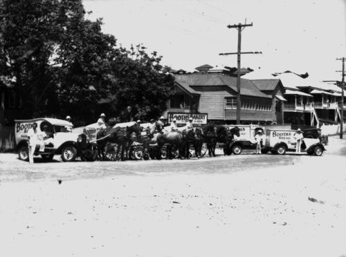 Bakery delivery trucks and horse carriages on a street.