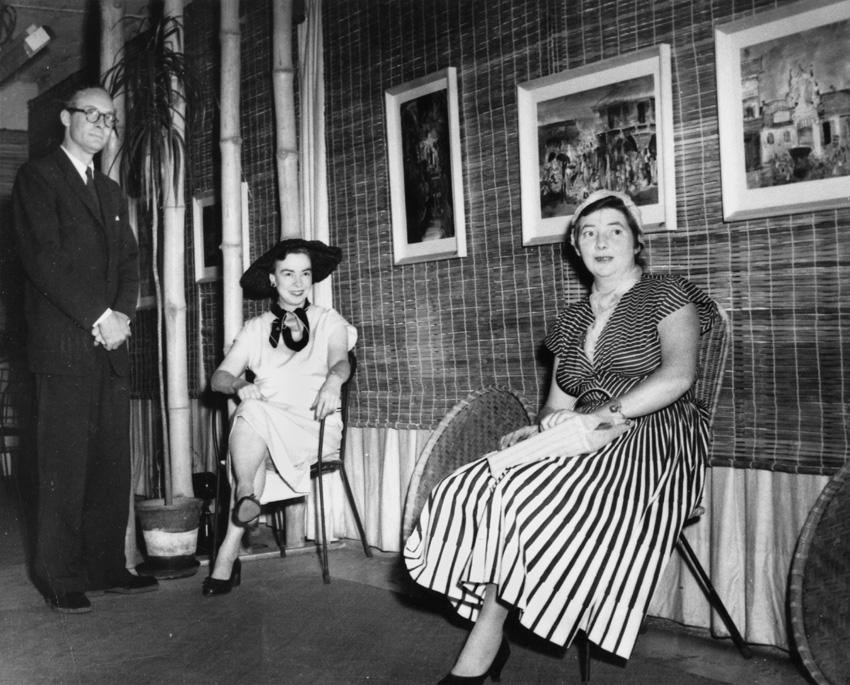 Black and white photo of two women seated and a man standing in a gallery. Brian and Marjorie Johnstone with Margaret Olley at The Johnstone Gallery in the basement of the Brisbane Arcade.
