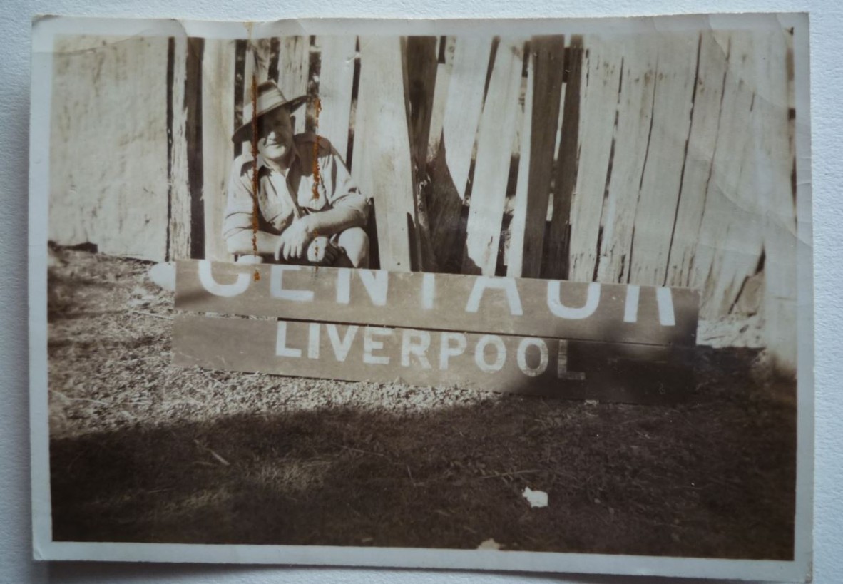 Man squatting behind Centaur Memorial Fund collection timber board