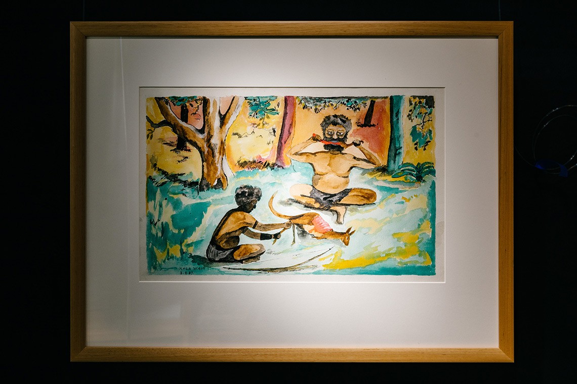 This watercolour painting by Kala Waia is entitled “Baira and Agburug (as man)” and illustrates the Torres Strait Islands legend of Agburug. The painting depicts Baira sitting cross-legged in a clearing in the bush eaing kangaroo meat with another man. The dead kangaroo is in the centre of the painting.