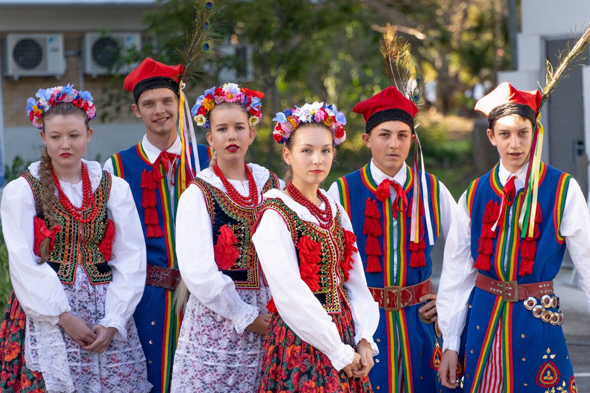 Members of Obertas Polish Folkloric Ensemble waiting to perform. They are dressed in colourful traditional Polish clothes, wearing flower crowns or peacock feathers.