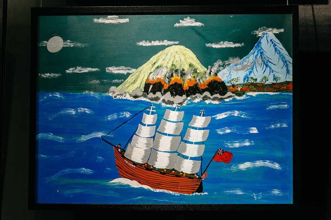 The painting, "Sail Away", depicts the First Nations’ oral history of Captain Cook’s landing at Endeavour River. The acrylic on plywood painting shows the night sky in the background with the mountains and land on fire. In the foreground is the ship Endeavour, flying the English flag, and sailing away.