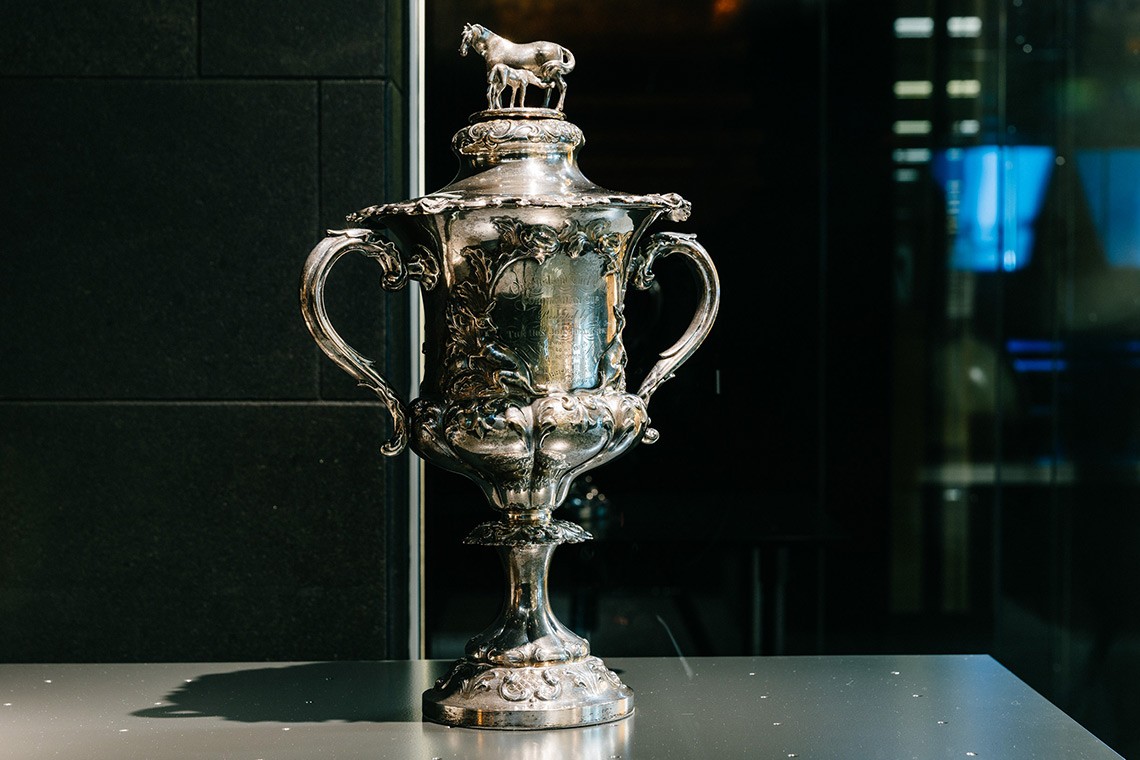 Sterling Silver Cup presented to Robert George Wyndham Herbert, first Premier of Queensland, whose horse won the Queensland Turf Club's Corinthian Handicap Race. The cup's cover features a modelled group of a horse and foal, and the body of the cup is decorated with images of horses, riders, and kangaroos.
