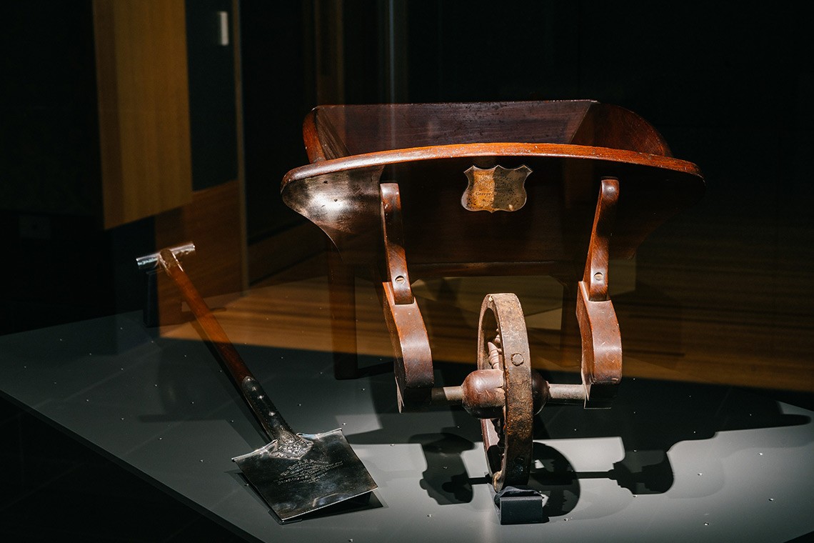 The presentation nickel silver spade and timber wheelbarrow were presented to Arthur Palmer, former Queensland Premier at a ceremony held to mark the turning of the first sod of the Sandgate Railway in 1881. The spade is engraved in large script on the front and is attached to a timber shaft which has a plain T shaped nickel handle. The model wheelbarrow is constructed from red cedar.