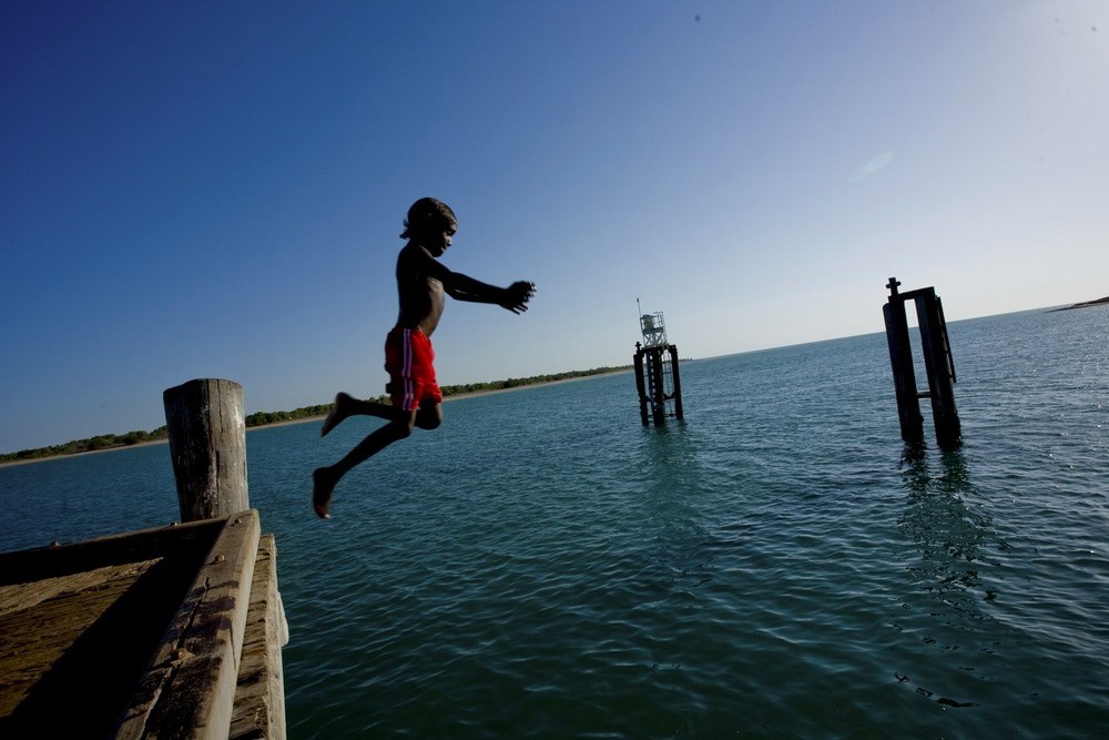 Young boy jumping from wharf into ocean