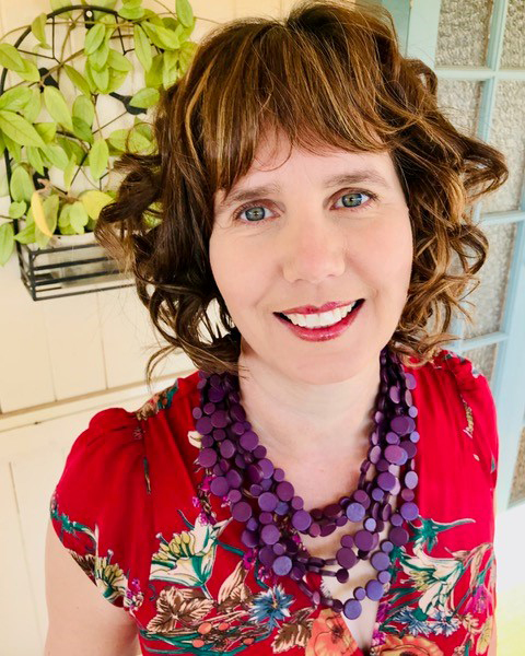 Tabitha Bird, in red dress with flowers and strings of purple beads