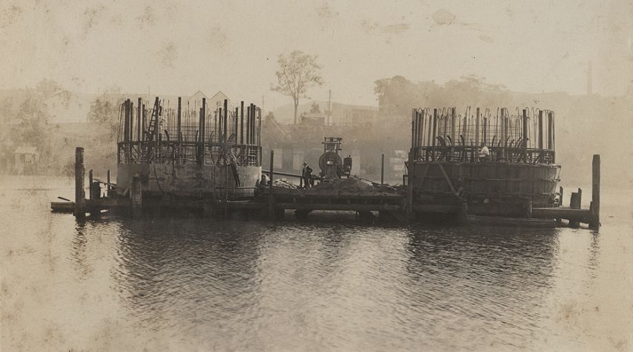 This photo, in the Album of the Queensland Cement & Lime Company Limited Photograph Albums, shows the caissons being built within the sand-island method. This innovative method was designed by Manuel Hornibrook for the unique requirements of sinking the pylons to the Brisbane River bed.