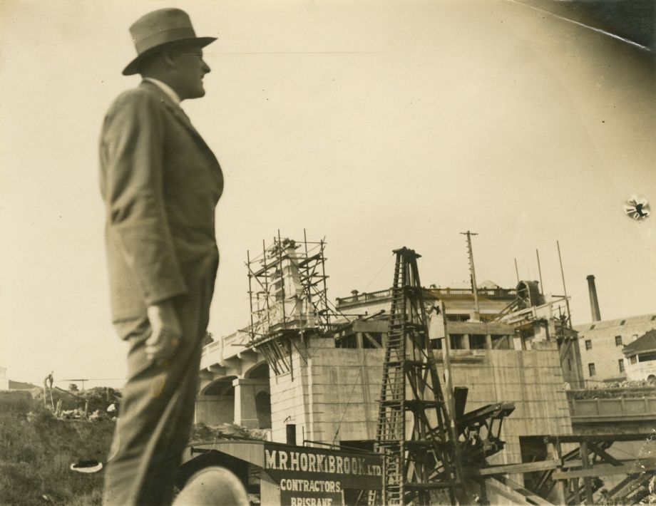 Photo taken of Manuel Hornibrook as he looks over building site of Grey St Bridge as pylon and approach to Bridge on north side is being built. MR Hornibrook Pty Ltd contractors sign in background.