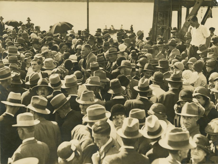 The image shows men and women mingling in the crowd at the opening of the Grey Street Bridge. Manuel Hornibrook, in centre of photo is one of the few men not wearing a hat on the day.
