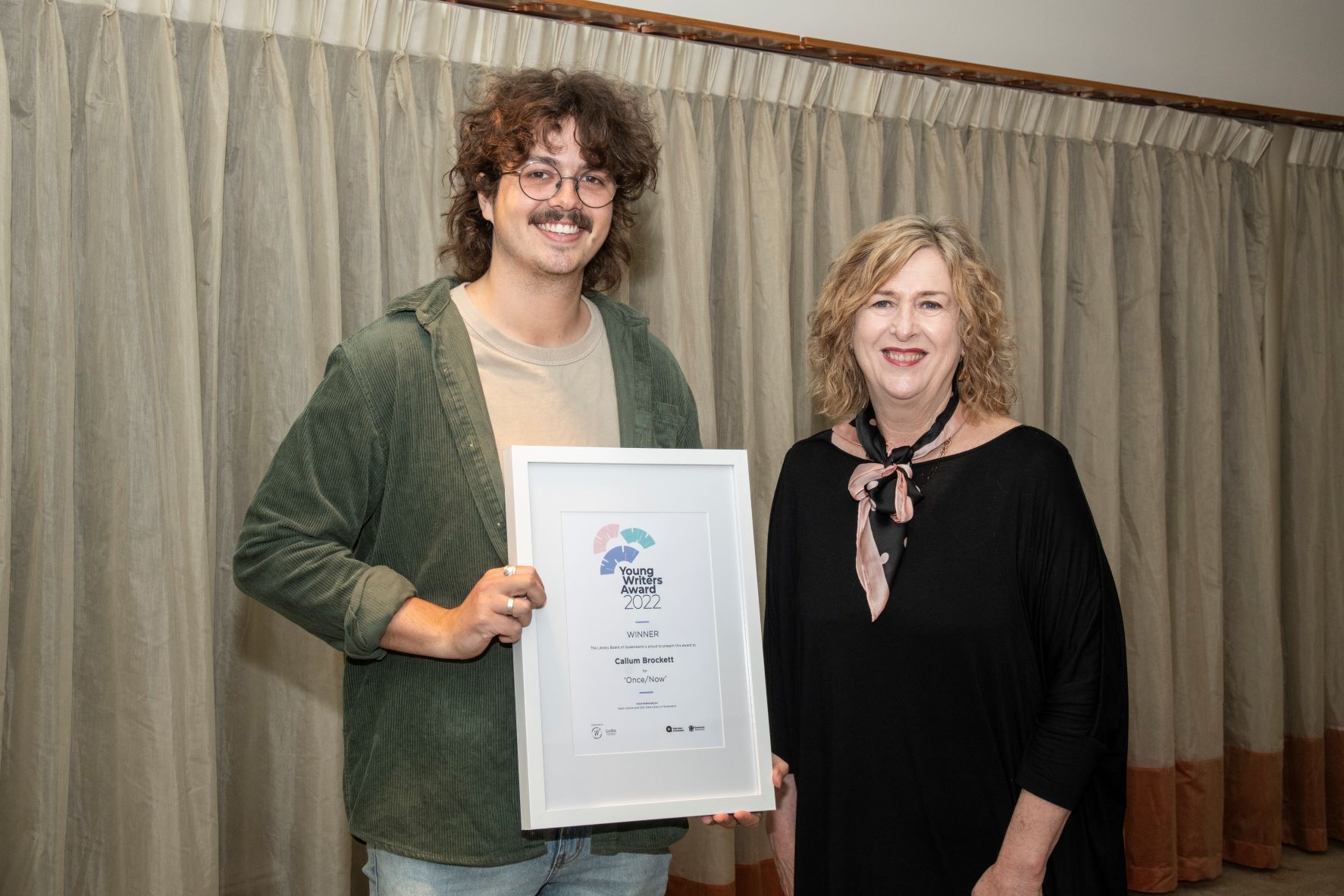 Two people standing next to each other smiling, one is holding a certificate